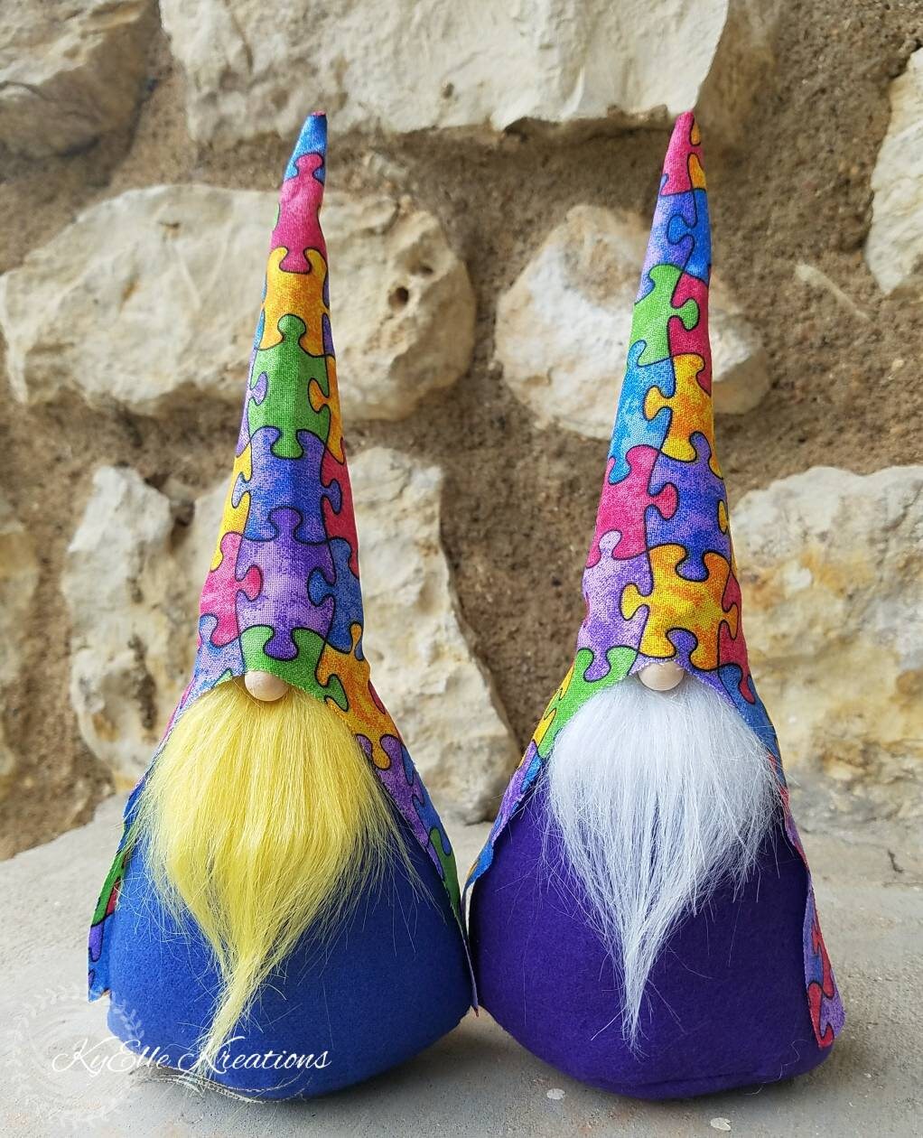 Autism Awareness Gnomes with colorful puzzle piece hats, one with yellow beard and blue body. The other shown with white beard and purple body.
