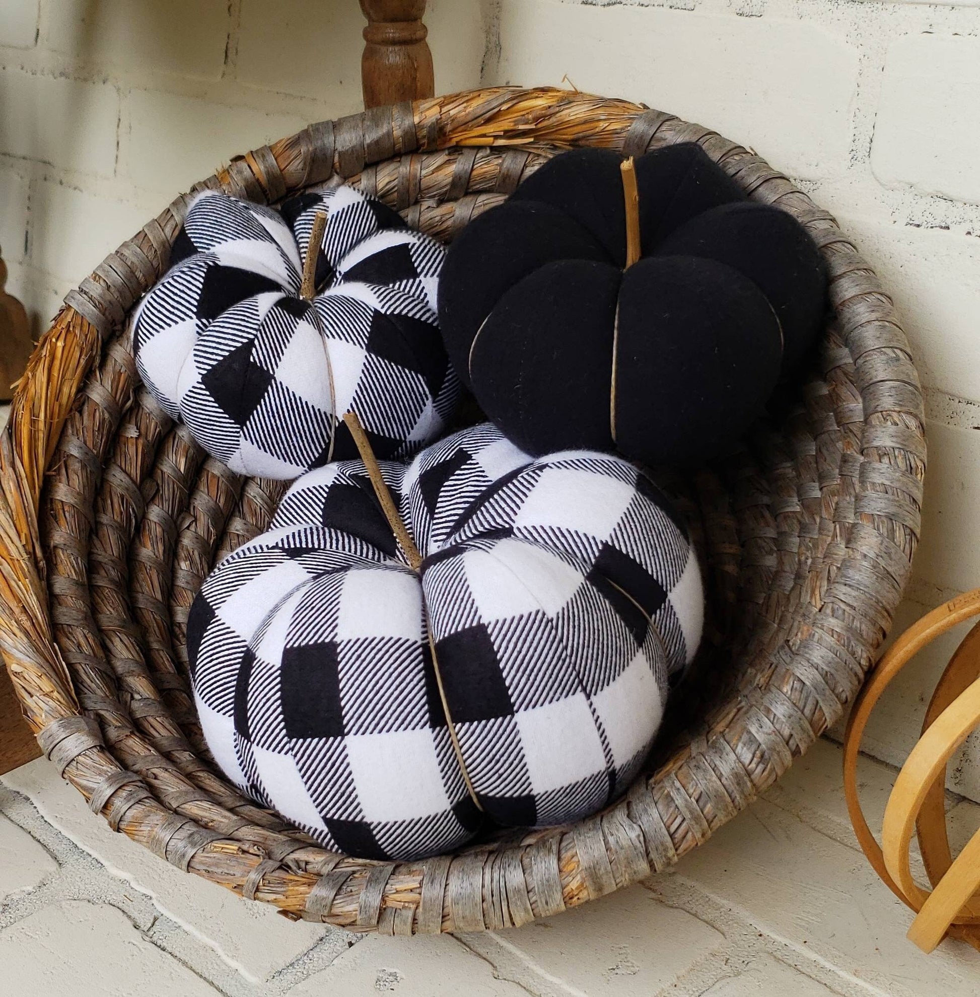 Black and white Buffalo plaid Halloween or Fall handmade fabric pumpkins. Trio comprised of one large and one small in plaid print, with third in solid black color. Displayed in hand woven basket.