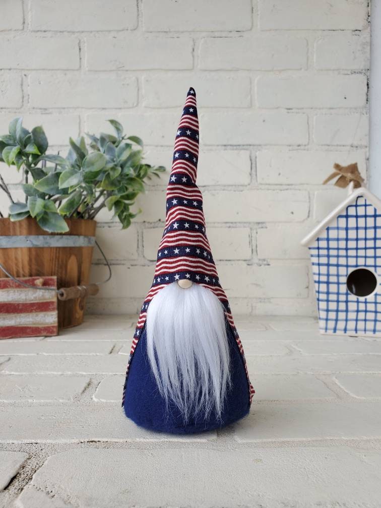 Patriotic Gnome with white beard. 9inch handmade KyElle Kreations home decor Gnome with primitive colored striped flag hat and navy body . Displayed with faux foliage and seasonal accent decor.