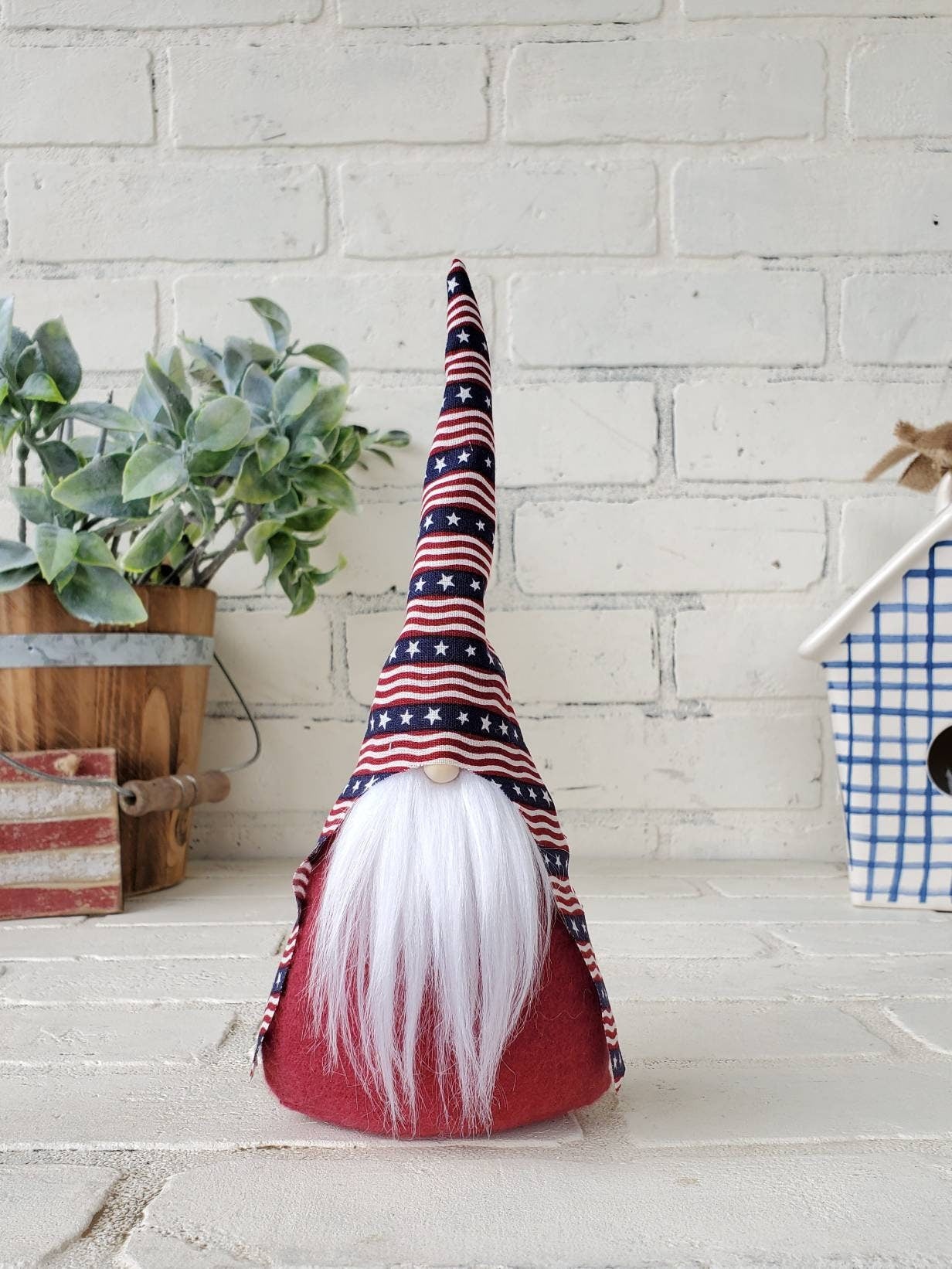 Patriotic Gnome with white beard. 9inch handmade KyElle Kreations home decor Gnome with primitive colored striped flag hat and burgundy body . Displayed with faux foliage and seasonal accent decor.