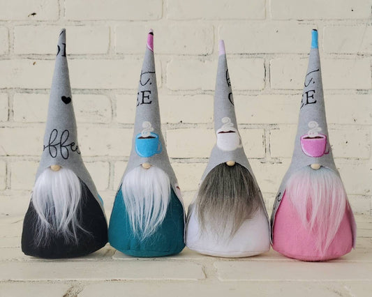 Coffee Gnome collection. With gray hats, adorned with coffee words and cups. In order with White beard and black body, white beard & teal body, gray beard & white body, lastly ombre beard & pink body. These handmade KyElle Kreations gnomes measure 9 inches.. Displayed with faux foliage and seasonal accent decor.