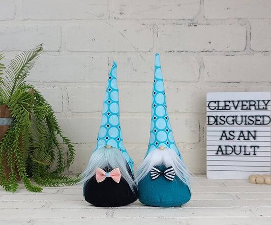 Bow tie Gnomes with lite blue & teal polka dot hats, one with lite blue beard & black body. Other with white beard & teal body. This handmade KyElle Kreations gnome measures 9 inches.. Displayed with faux foliage and seasonal accent decor.
