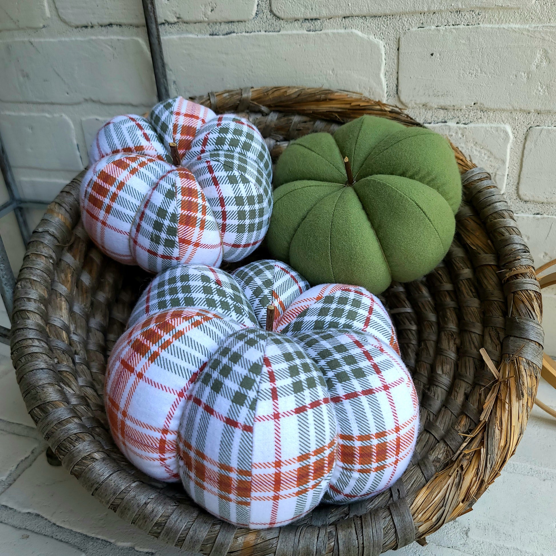 Pumpkin trio set in Fall plaid colors of burnt orange, sage and white. With one large and one small in plaid with one solid in sage color. Displayed in hand woven basket