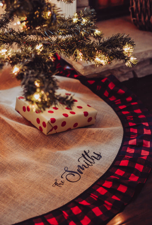 Red & Black Buffalo Plaid, Burlap Christmas Tree Skirt displayed below a lit decorated Holiday Tree. with gifts.