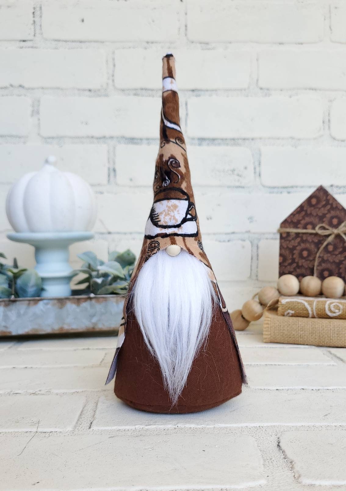 Coffee Gnome with white beard & brown body. This handmade KyElle Kreations gnome measures 9 inches.. Displayed with faux foliage and seasonal accent decor. 
