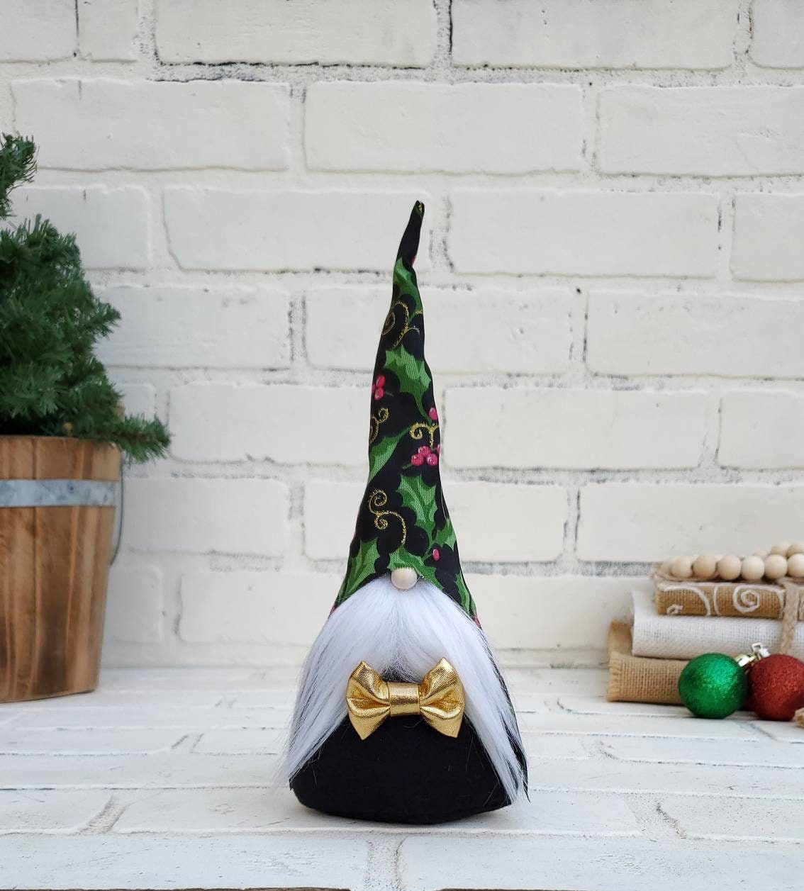 Christmas Holly Gnome with white beard & black body. Complete with gold bow tie. This handmade KyElle Kreations gnome measures 9 inches.. Displayed with faux foliage and seasonal accent decor.
