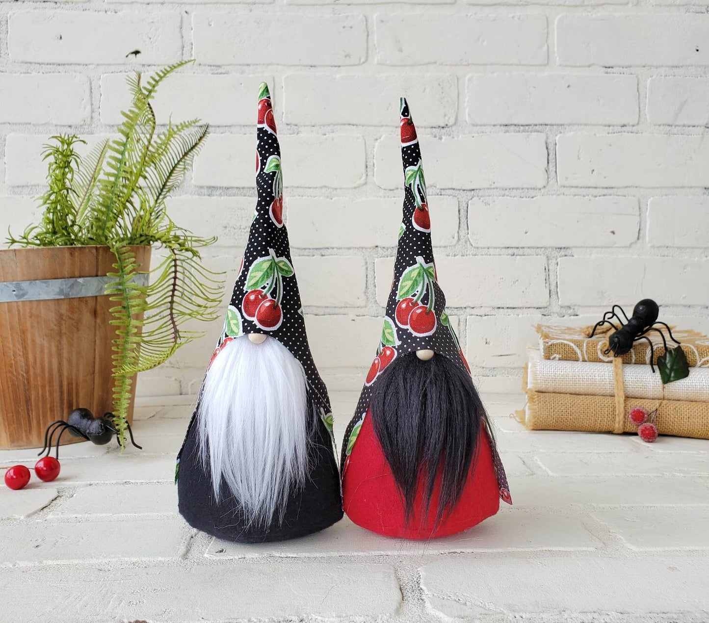 Cherry Gnomes with Black polka dot hat with cherry print. One with white beard & black body. Other has a black beard with red body. This handmade KyElle Kreations gnome measures 9 inches.. Displayed with faux foliage and seasonal accent decor. 