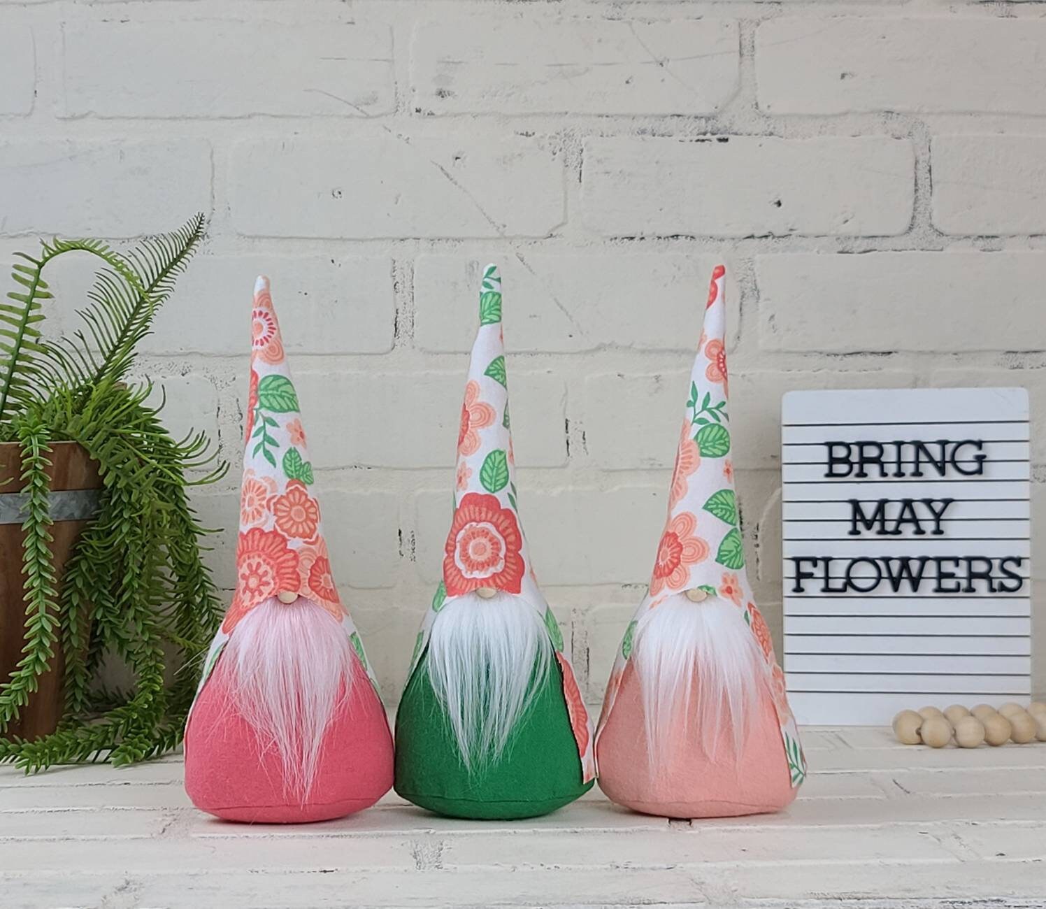 Floral Gnome collection. With peach and coral floral patterns. First with lite pink beard & coral body, second with white beard & green, lastly white beard with peach body.ith beard &  body. This handmade KyElle Kreations gnome measures 9 inches. Displayed with faux foliage and seasonal accent decor. 